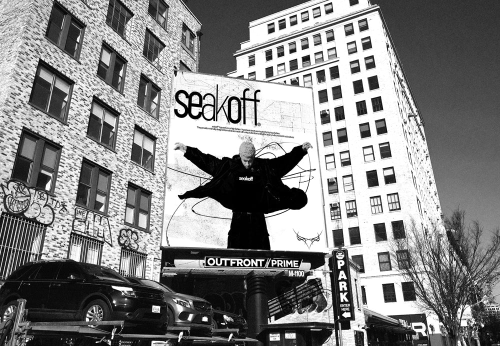 Black and white image of a city scene featuring a large billboard with the text "sealoff" and a person with arms outstretched in front of a graffiti-style background. Surrounding buildings have visible graffiti on some walls.