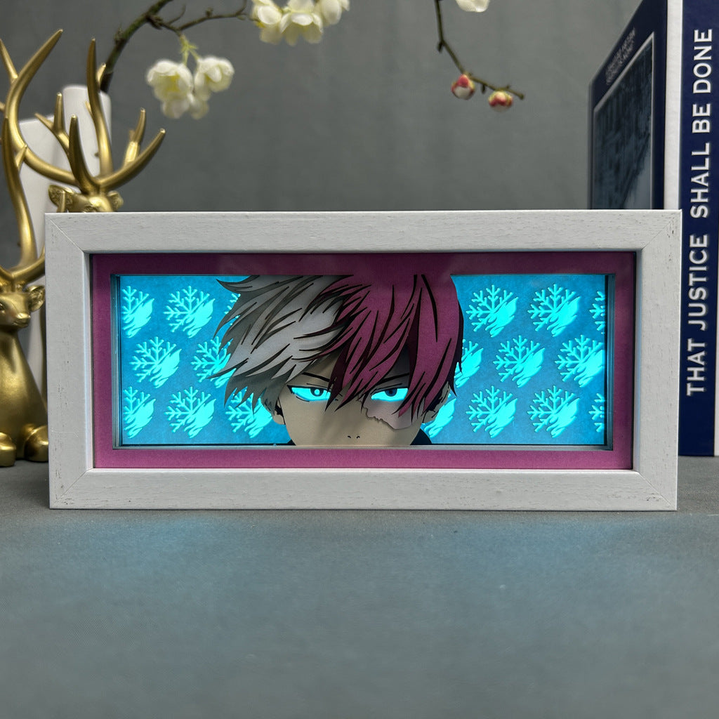 The My Hero Academia Anime Light Box features a 3D effect of Shoto Todoroki with red and white hair against a vibrant teal leaf-patterned background, blue eyes, and adjustable 16-color LED lights. It sits elegantly on a gray surface among decorative items.