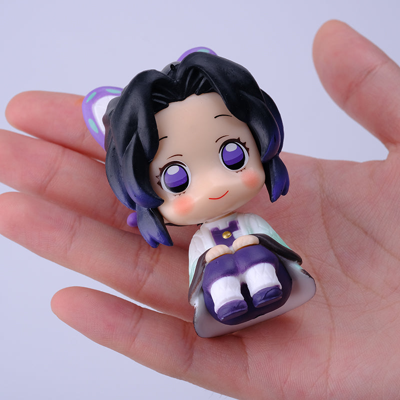 A hand holds a small chibi-style figurine from the Demon Slayer Figure Set, featuring large purple eyes and black hair in a white and purple outfit, ideal for any anime collection inspired by Demon Slayer: Kimetsu no Yaiba.