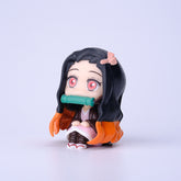 The Demon Slayer Figure Set includes a 7cm figure of a character with long black hair, red eyes, and a green object in her mouth. Dressed in pink and brown and sitting cross-legged, this is perfect for any Demon Slayer: Kimetsu no Yaiba anime collection.