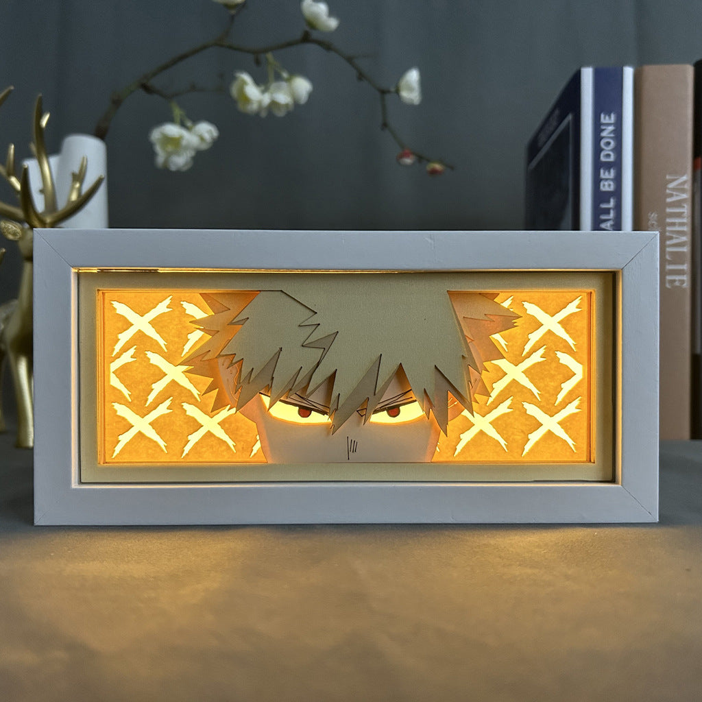 A My Hero Academia Anime Light Box features Katsuki Bakugo with spiky hair and intense eyes against a glowing orange X-pattern background, enhanced by a 3D effect. Alongside stands a decorative deer figure and books, highlighting the anime artwork. The LED light offers 16 adjustable colors.