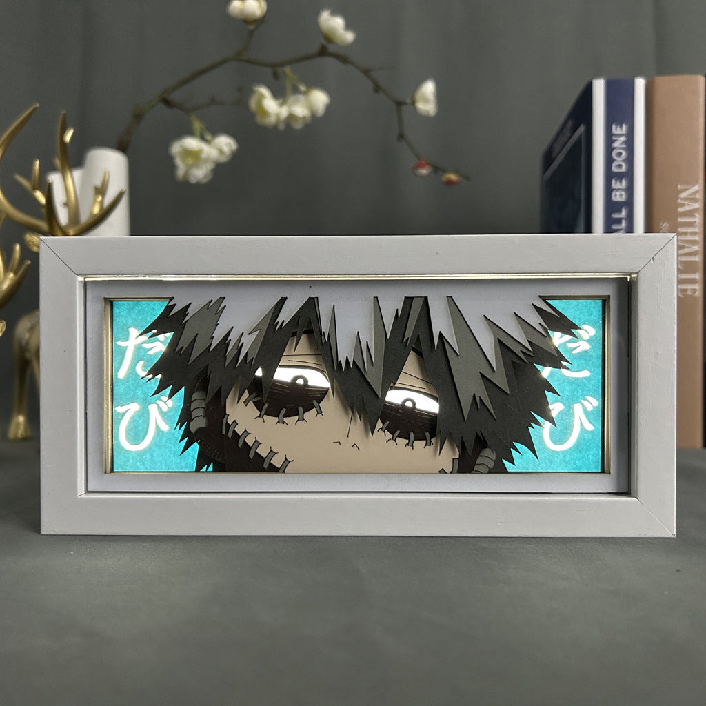 A My Hero Academia Anime Light Box featuring a 3D effect of Dabi, with stitched skin and dark hair against a blue backdrop with Japanese text. Encased in a white frame, this 16-color adjustable LED light box adds style among decorative items and books.