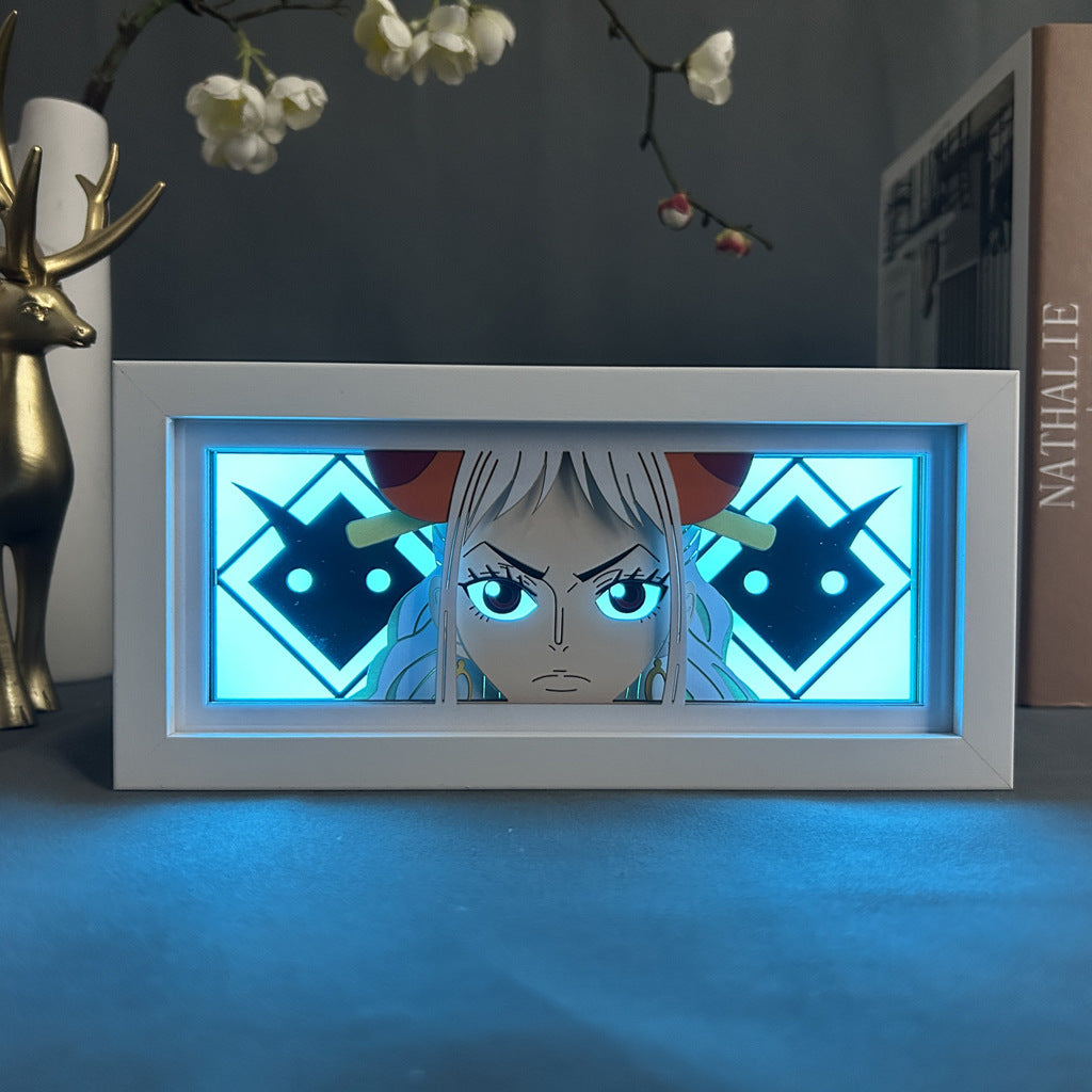 The Seakoff Yamato One Piece 3D LED Light Box, an anime collectible lamp with 16 colors, showcases a character with long hair and horns against a blue geometric background. Nearby, a deer figurine and the book "Nathalie" enhance the anime-themed decor.