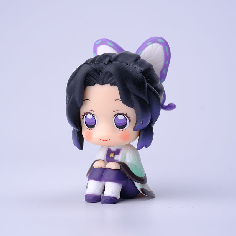 A small figure of a character with black hair, purple eyes, and butterfly-themed accessories sits cross-legged. Wearing a purple and white outfit with a gentle smile against a plain light background, it’s part of the Demon Slayer Figure Set - 7cm 8-Piece Solid PVC Anime Figures collection.