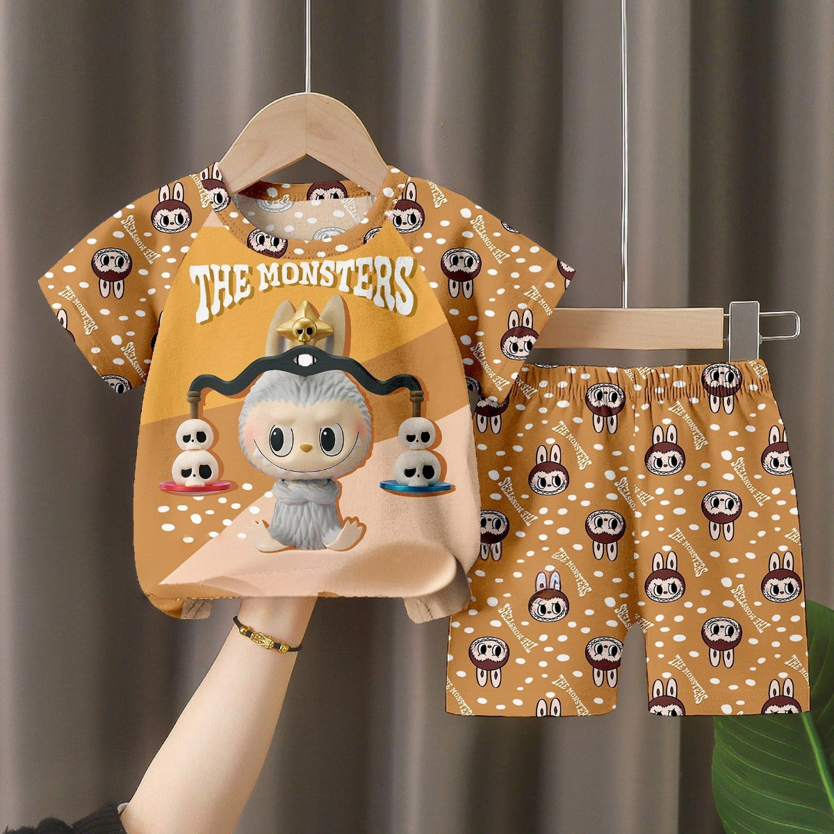 The LABUBU Baby Pajama Set - "The Monsters" features a playful monsters theme, with a light brown short-sleeve shirt and shorts, made from milk silk. The shirt highlights a large toy-like monster graphic and the whimsical text "The Monsters.