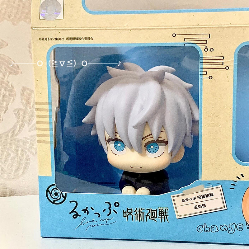 A cute 12cm Gojo Satoru figure from Jujutsu Kaisen, featuring gray hair, blue eyes, and a seated pose with arms on knees. Packaged in light blue and beige box adorned with decorative designs and Japanese text. Brand: Jujutsu Kaisen.