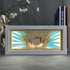 The Seakoff Dragon Ball Z Anime Light Box showcases Super Saiyan Goku in 3D with spiky hair and glowing eyes against a vibrant background. It’s encased in a white frame on a table next to gold deer figurine, books, and white flowers, offering a 16-color adjustable LED light display.
