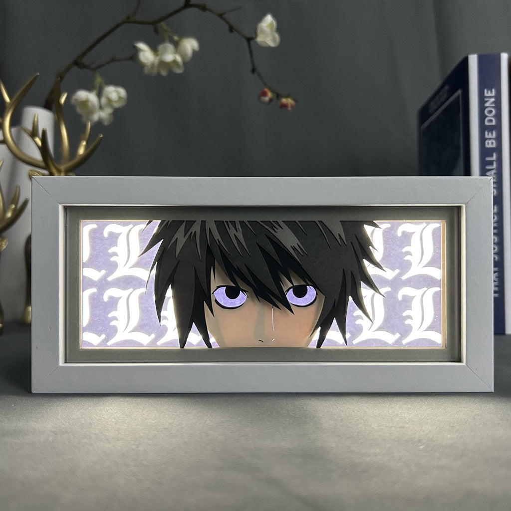 The Death Note Anime Light Box, featuring L (Lawliet) in anime-style with dark hair and purple eyes, includes a 3D-effect white "L" pattern background. A decorative floral branch and book enhance the scene. This 16-color adjustable LED light is a product of the Death Note brand.