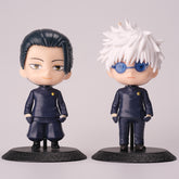 Two chibi-style figures from the Gojo Satoru & Suguru Geto 10-Piece Action Figure Set by Jujutsu Kaisen are displayed. The left figure resembles Suguru Geto with dark hair, while the right features Gojo Satoru with white spiky hair and blue glasses. Both figures are in dark attire.