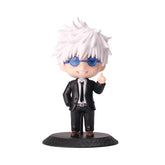 A 10cm chibi-style Gojo Satoru figure, from the Jujutsu Kaisen action figure set, features spiky white hair, blue glasses, and a sleek black suit with a tie. Standing on a textured black base, this collectible displays a smiling expression and playful hand gesture.