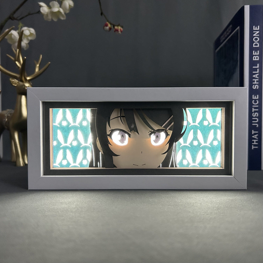 The Seakoff OreGairu Anime Light Box features a 3D effect illustration of Yukino Yukinoshita with large eyes, illuminated by 16-color adjustable LEDs, against a geometric pattern. A deer figurine and book add depth to the scene, enhancing your decor.