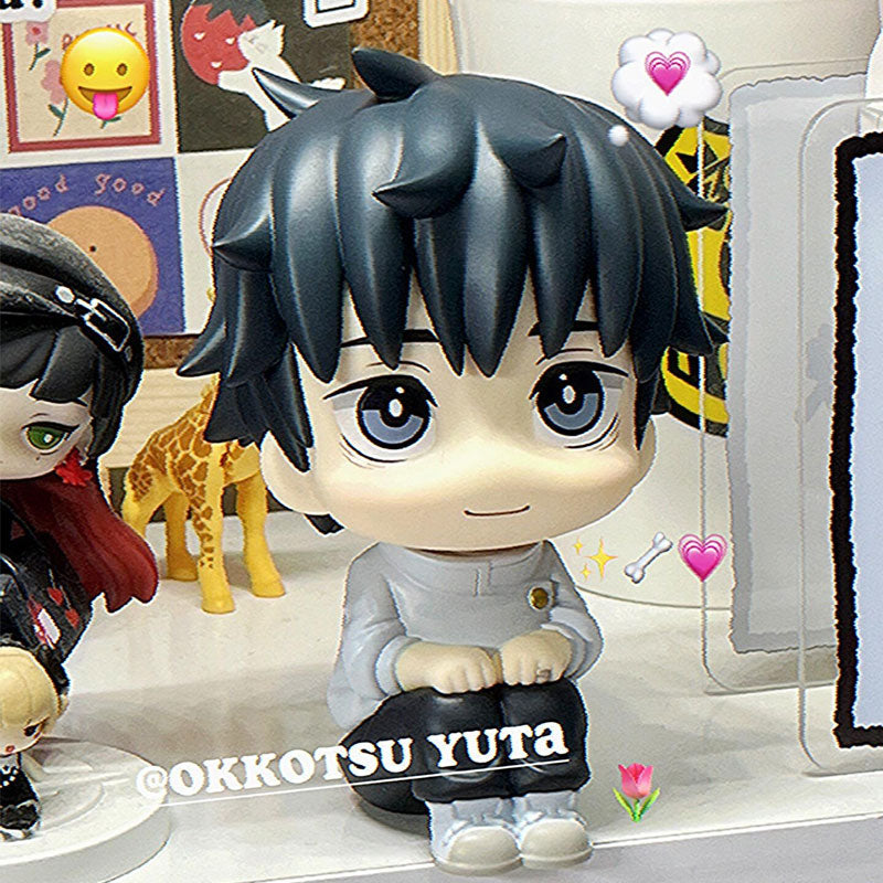 A Yuta Okkotsu figure from the Jujutsu Kaisen collection sits on a shelf in light attire. A small giraffe toy and another chibi figure with dark hair and a hat are nearby. Emoticons like hearts and a dog bone float around, with the handle "@okkotsu_yuta" visible.