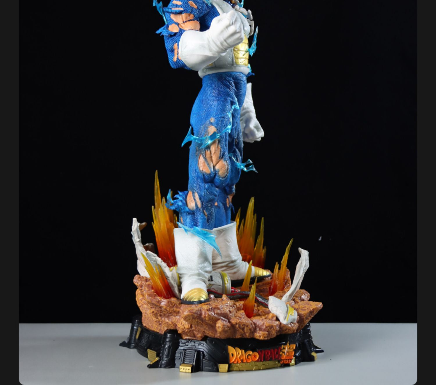 The Seakoff Vegeta Collectible Figure, 55cm tall, showcases a striking Super Saiyan form. It features three interchangeable heads (Super Saiyan, Super Saiyan Blue, and Normal forms) on a rocky base with flame-like details and "Dragon Ball Z" displayed. The vivid design pops against the black background.