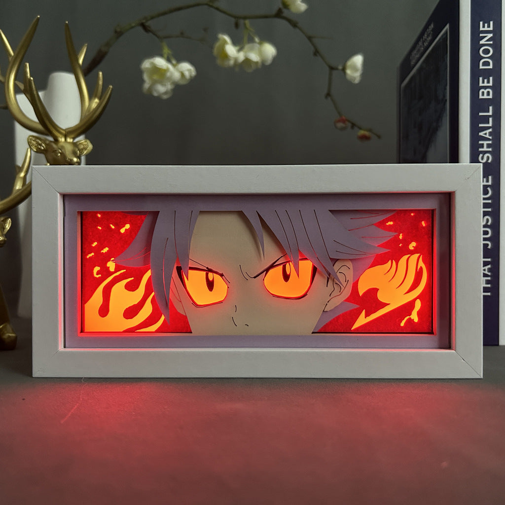A framed artwork of an anime character with glowing red eyes against a fiery backdrop. Ideal for anime lovers, it mirrors the dynamic flair of the Fairy Tail Natsu Dragneel LED Light Box - 3D Fairy Tail Anime Lamp, set amidst decorative branches and books.