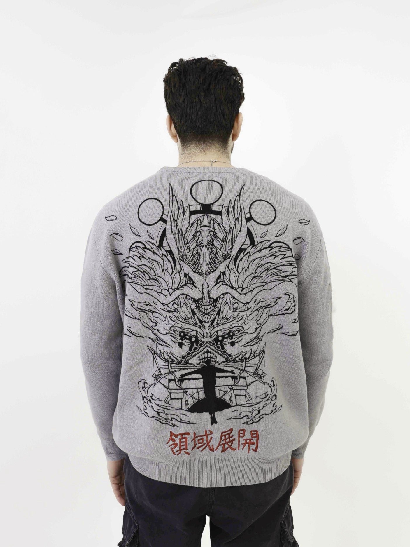 A person with short dark hair is turned away, wearing the Premium Jujutsu Kaisen-Inspired Knit Sweater by Jujutsu Kaisen, featuring a jacquard design of a dragon and temple. Circular symbols hover above the dragon with red Asian characters below, echoing anime streetwear styles.