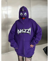 With its trendy streetwear vibe, the oversized purple Seakoff hoodie features a fun cartoon face on the hood with eyes and a smile. "Anazzy" is boldly printed in white on the front as it zips up against a metallic wall backdrop.