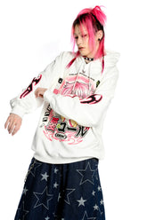 A person with pink hair in braided pigtails is wearing the Seakoff Y2K Aesthetic Anime Hoodie, a retro manga girl graphic pullover with kawaii phone design. Their dark star-patterned pants enhance their Y2K style against a crisp white background.