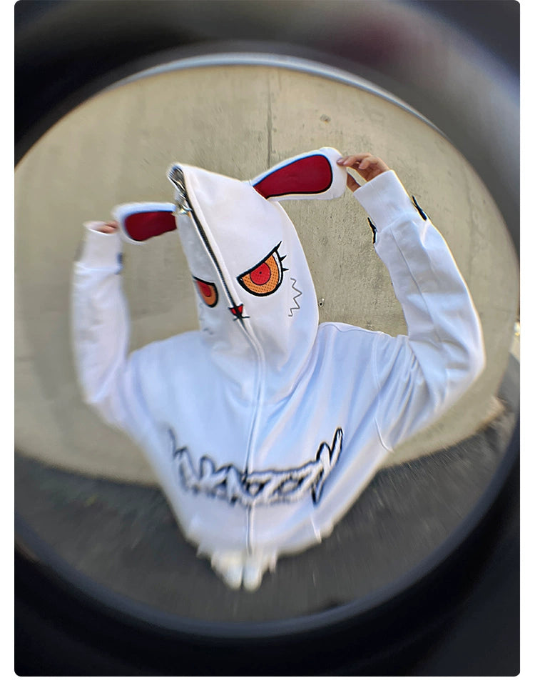 Wearing the Seakoff Fierce Bunny Hoodie, made of 400GSM cotton with red-eared and large-eyed design, someone is captured in a fisheye lens shot, set against a concrete wall.
