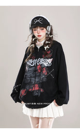In front of a plain background, someone shows off their alternative style with the Seakoff Gothic Hello Kitty Princess Hoodie featuring edgy heart and cross graphics, paired with a white pleated skirt and a black cap adorned with a bow. Headphones over small hair bows complete the kawaii look.