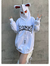 Against a concrete backdrop, someone in a Seakoff Fierce Bunny Hoodie with red-eyed rabbit ears and bold black design makes peace signs. The oversized 400GSM cotton hoodie adds edge with zipper details and subtle stitching.
