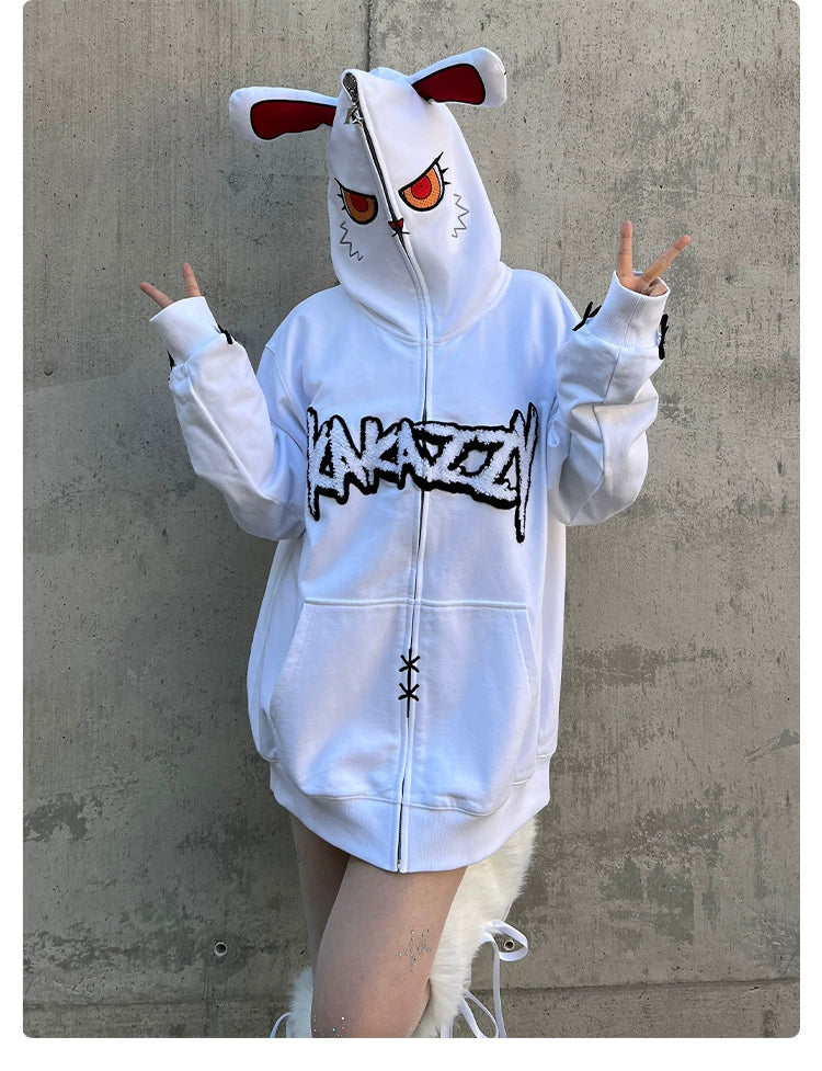 Against a concrete backdrop, someone in a Seakoff Fierce Bunny Hoodie with red-eyed rabbit ears and bold black design makes peace signs. The oversized 400GSM cotton hoodie adds edge with zipper details and subtle stitching.