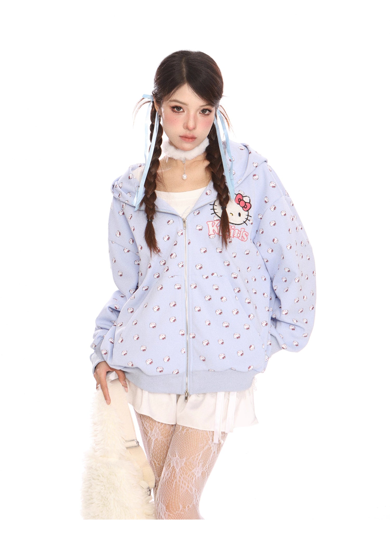 A young woman stands against a white background in kawaii fashion, wearing a Seakoff Hello Kitty Pink Kawaii Hoodie featuring cat ears and Sanrio prints. Paired with a white skirt, lace-patterned tights, braided pigtails, she holds a fluffy white bag.