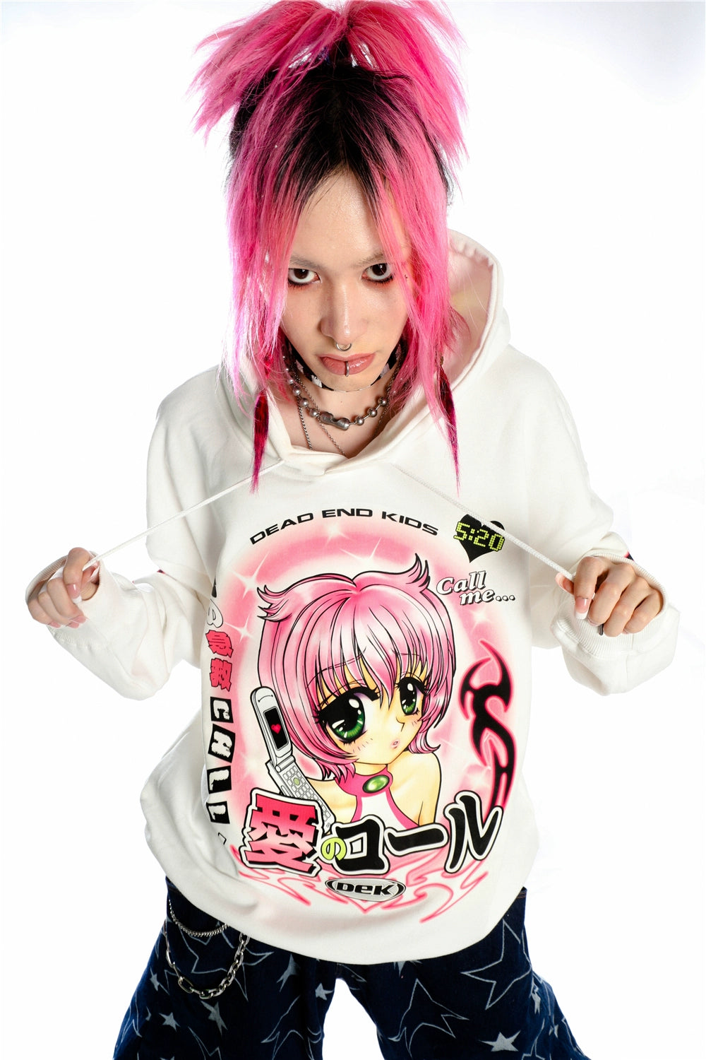 A person with pink hair poses playfully in a Seakoff hoodie, adorned with a retro manga girl featuring large eyes and matching pink hair. The Y2K aesthetic anime design on the pristine white background adds an extra touch of kawaii style flair.