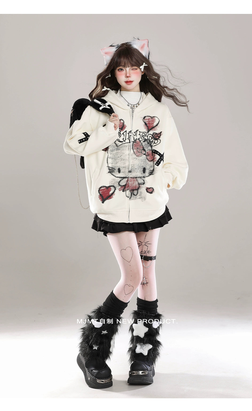 A person in a white Seakoff Gothic Hello Kitty Princess Hoodie, featuring edgy heart and cross graphics, poses against a plain background embodying kawaii fashion. They wear a black skirt, furry black leg warmers, a cat ear headband, and have long hair. Their arms are slightly spread with legs crossed at the ankles.