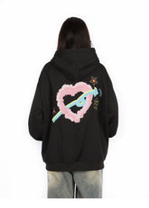 A person with long hair is wearing a Seakoff Kawaii Pastel Cartoon Hoodie featuring playful pink heart, blue ribbon, star, and flower designs on the back. Embracing kawaii fashion, they&