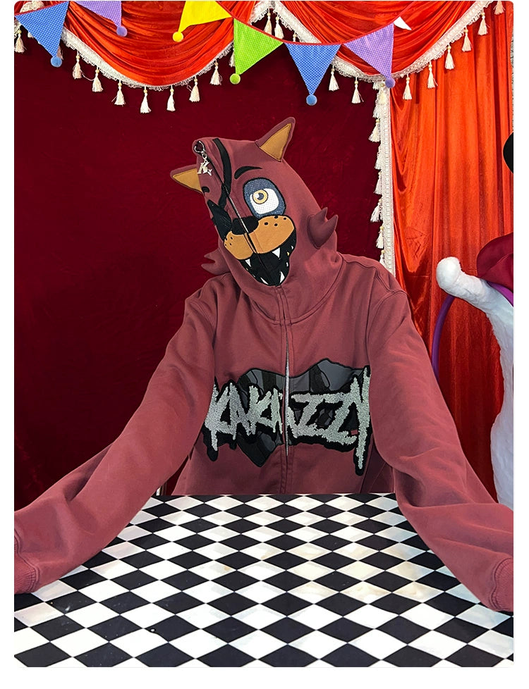 A person in a red Seakoff Foxy-Inspired Hoodie, featuring an animal face and ears with "KNAYZZZ" text, sits at a checkered table. Ideal for Five Nights at Freddy&