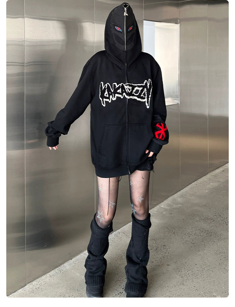 A person indoors wears a Berserk-Inspired Griffith Dark Knight Hoodie, a 400GSM black zip-up oversized streetwear by Berserk. The hood obscures their face. They pair it with sheer leggings featuring designs and black leg warmers, against a metallic wall and concrete floor backdrop.
