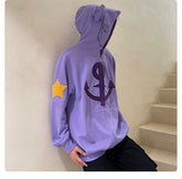 A person wearing a Seakoff Purple Symbol Hoodie—an oversized 400GSM anime zip-up with an anchor, a star on the sleeve, and ear design—stands by a beige stairway. With the hood up, their face is concealed, making this streetwear pop against the plain light-colored background wall.