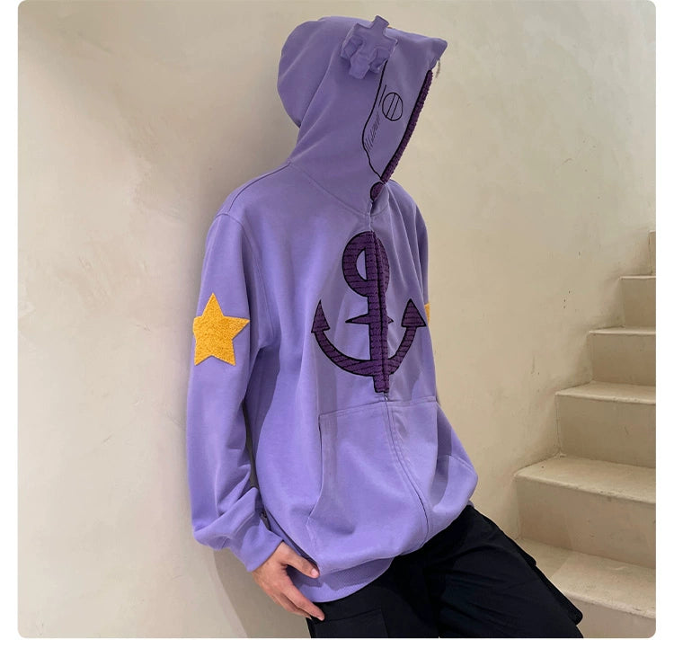 A person wearing a Seakoff Purple Symbol Hoodie—an oversized 400GSM anime zip-up with an anchor, a star on the sleeve, and ear design—stands by a beige stairway. With the hood up, their face is concealed, making this streetwear pop against the plain light-colored background wall.