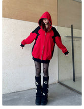 A person poses against a beige wood-paneled wall, wearing the Seakoff Deadpool-Inspired Hoodie—a red and black oversized zip-up superhero sweatshirt—with the hood on, star-patterned tights, and black boots. Their slightly outstretched arms create a bold look as they gaze forward.