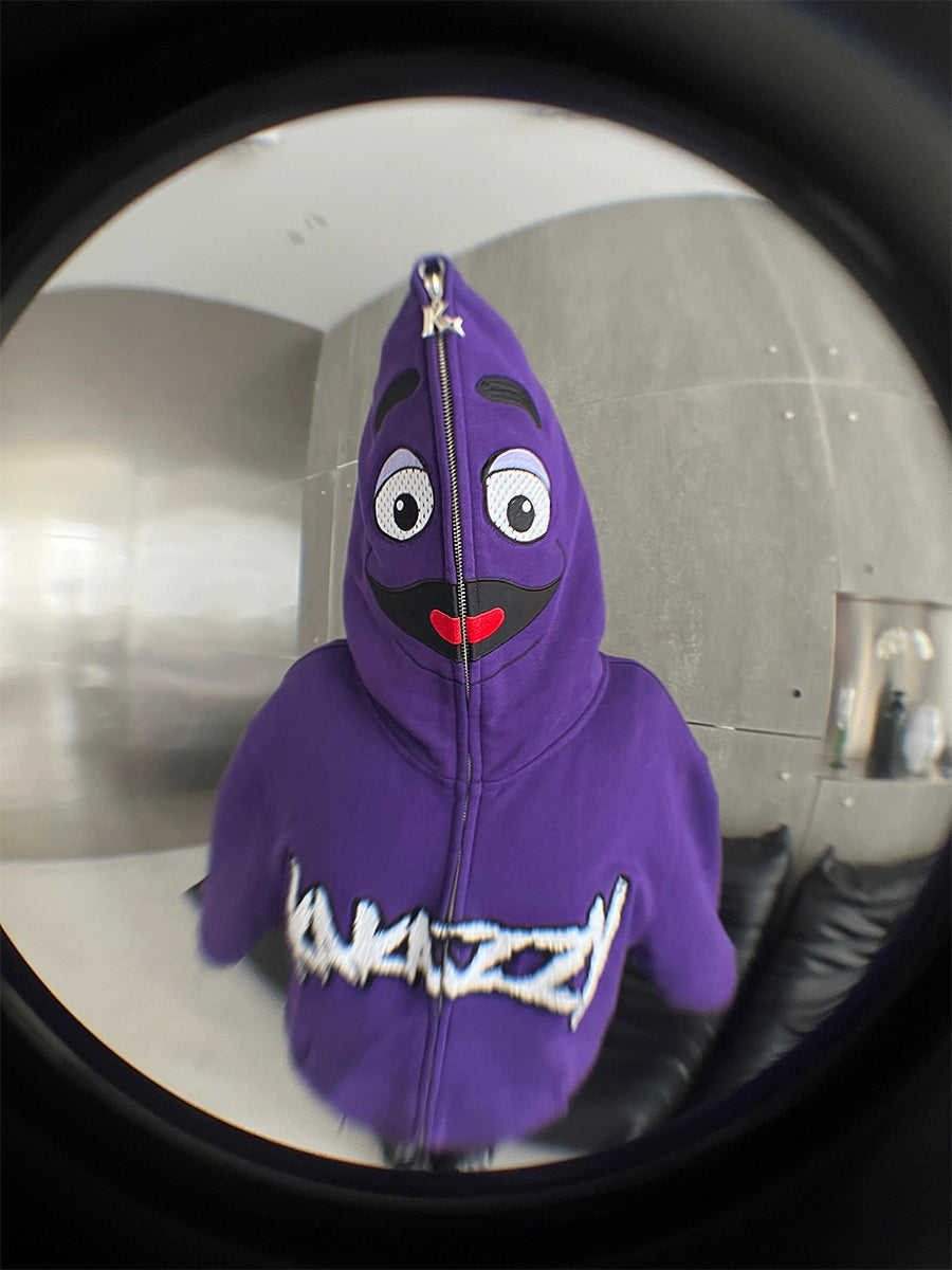 Styled in an oversized Fun Cartoon Face Hoodie by Seakoff—complete with large eyes, a smile, and a mustache—this purple 400GSM zip-up sweatshirt offers streetwear flair. Captured with a fisheye lens for playful distortion, it exudes a bold and whimsical vibe.