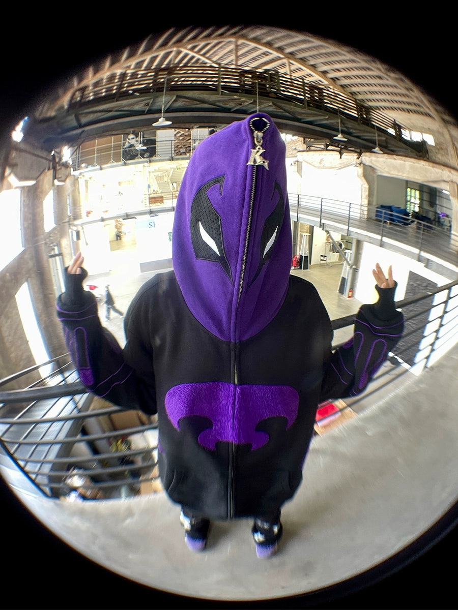 A person poses indoors wearing the Seakoff Dark Hero Hoodie, a black and purple oversized 400GSM streetwear zip-up with stylized markings. The fisheye lens effect distorts the image while they flash peace signs against an industrial backdrop.
