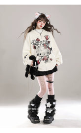 A person with long hair against a plain background showcases kawaii fashion, donning cat ears, a Seakoff Gothic Hello Kitty Princess hoodie featuring edgy heart and cross graphics, a black pleated skirt, heart-patterned white tights, furry boots, and holding a plush toy for an alternative playfulness.