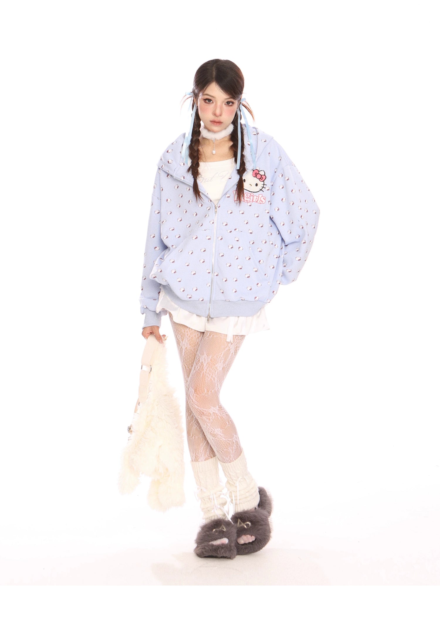 Against a white backdrop, a person embodies kawaii fashion in a Hello Kitty pink hoodie by Seakoff, featuring cat ear accents and all-over prints. They wear white shorts, lace-patterned tights, hold a plush toy, and complete the adorable look with grey slippers and two braided hairstyles.