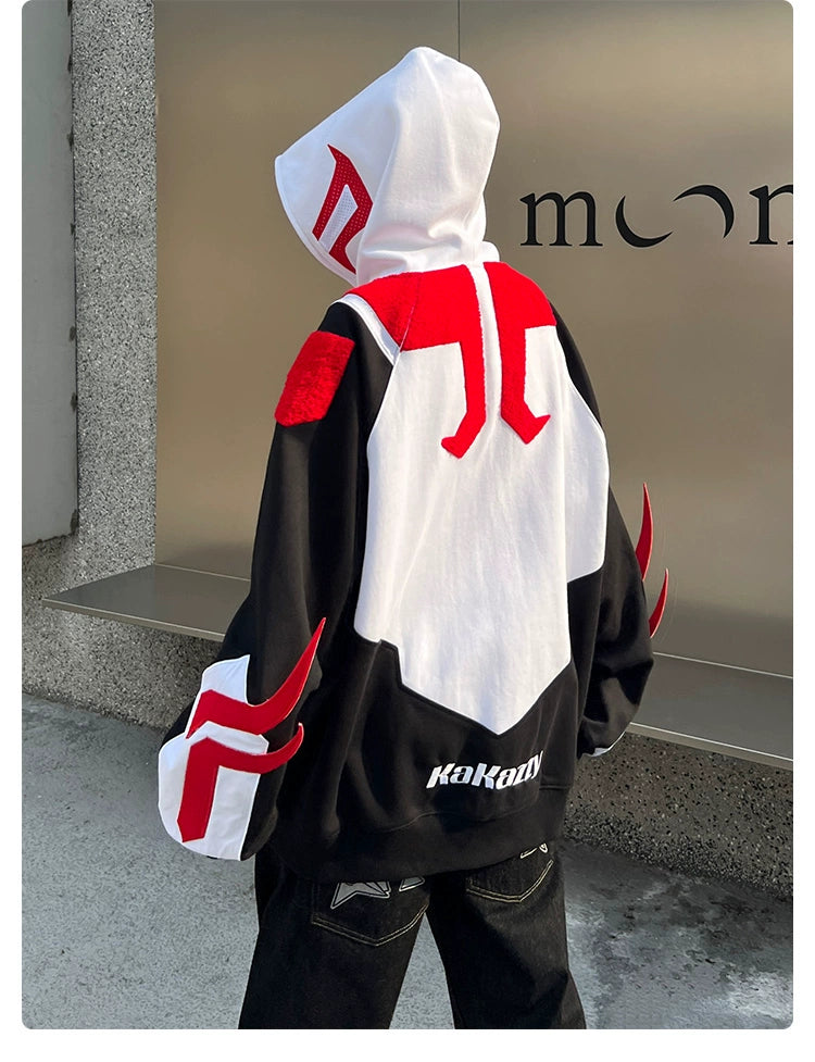 A person in a Seakoff Superhero-Inspired Hoodie poses by a wall with partial "moon" text. Their 400GSM oversized streetwear sweatshirt, ideal for comic book fans and fashion enthusiasts, boasts bold red and white patterns with "KaKaoix" near the hem.