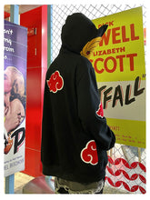 Wearing a Seakoff Uchiha Obito-Inspired Hoodie featuring the Akatsuki Cloud Design and Spiral Mask, a person stands back to the camera near a movie poster and chain-link fence in a colorful room, sure to capture any Naruto fan&