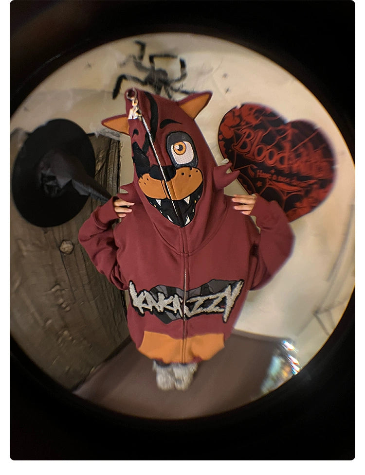 A person is wearing an oversized red Foxy-inspired hoodie from Seakoff, featuring a cartoon animal on the hood. The backdrop includes a black witch hat and a heart-shaped object with "Blood" on it, giving off Five Nights at Freddy&