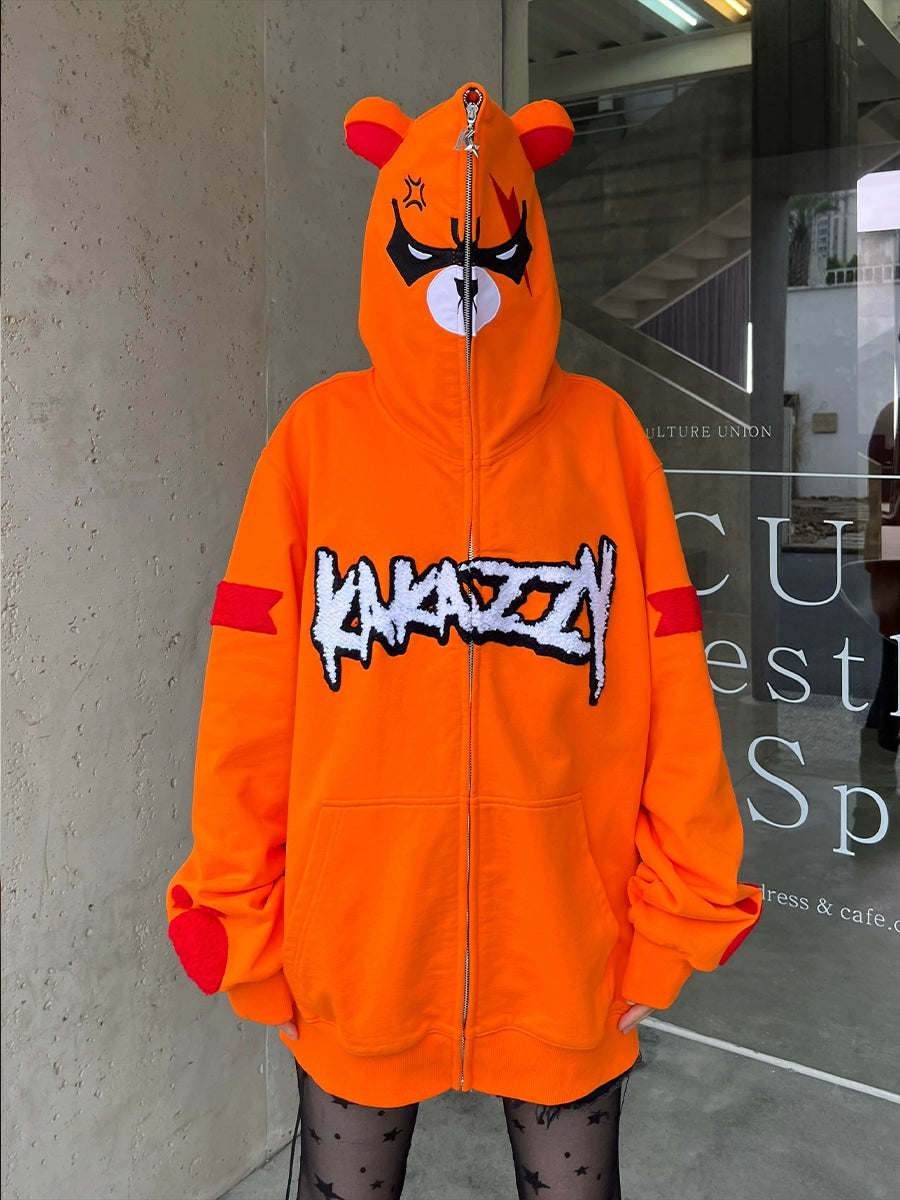 A person stands by a glass-windowed building wearing the Seakoff Furious Orange Bear Hoodie, crafted from premium 400GSM cotton. The hoodie features an angry bear face on the hood, "KRAZY" text, and red sleeve embroidery.