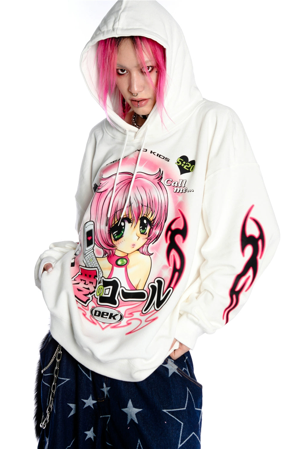 A person with pink hair wears a Seakoff Y2K Aesthetic Anime Hoodie featuring retro manga graphics and kawaii phone designs. Their dark pants, complete with a chain, add to the Y2K vibe as they gaze at the camera.
