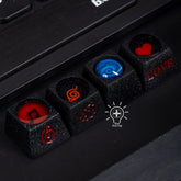 Close-up of black custom keycaps made from premium resin, featuring designs like a red music note and heart, orange swirl, blue vortex, and "LOVE" in red. Titled "The keycap," these are perfect for Naruto fans wanting a distinctive touch to their elements-themed keycap set.
