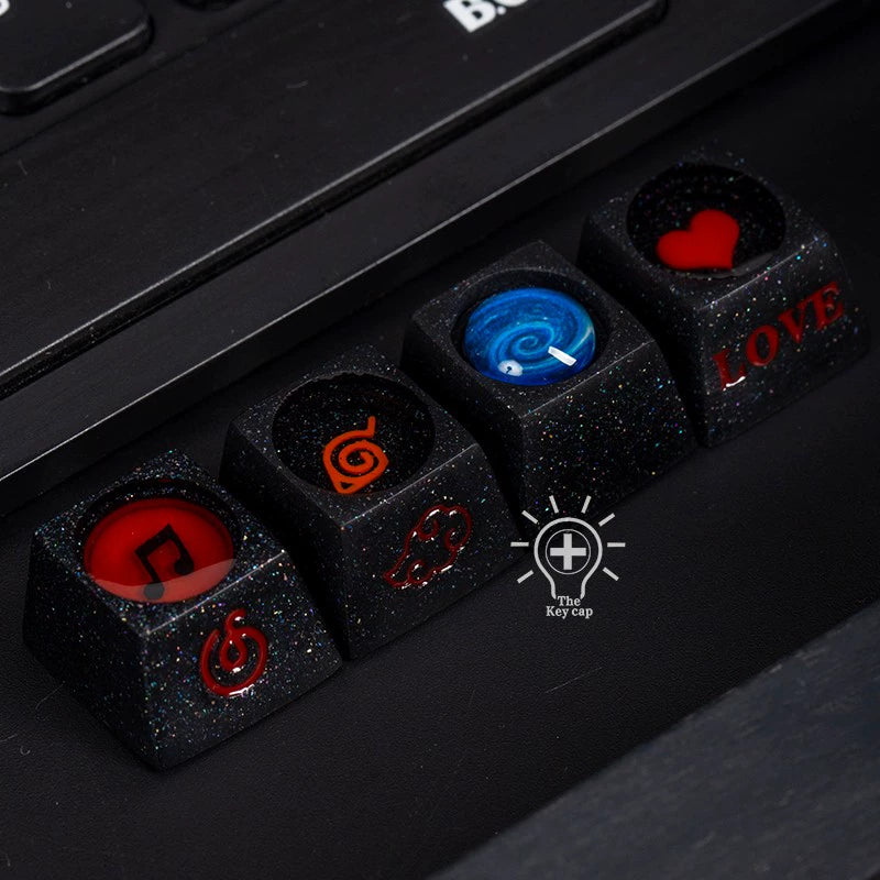 Close-up of black custom keycaps made from premium resin, featuring designs like a red music note and heart, orange swirl, blue vortex, and "LOVE" in red. Titled "The keycap," these are perfect for Naruto fans wanting a distinctive touch to their elements-themed keycap set.