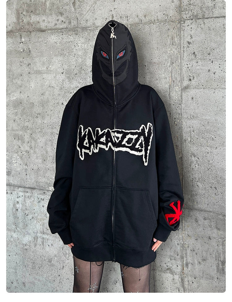 Wearing a black Berserk-Inspired Griffith Dark Knight Hoodie, zipped up to cover their face, the person stands against a concrete wall. The oversized streetwear features bold graphics and red sleeve symbols, paired with patterned tights for a Griffith-inspired look.