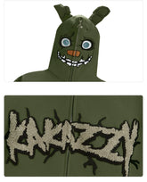 The Seakoff Springtrap-Inspired Hoodie is an oversized green zip-up sweatshirt featuring a cartoonish monster face with big eyes and sharp teeth, ideal for horror game fans. The lower part boldly displays "KAKAZZY." Perfect for lovers of Five Nights at Freddy&