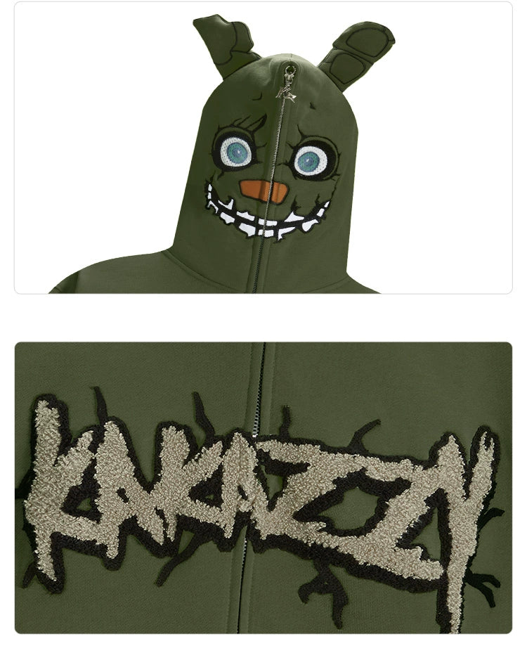 The Seakoff Springtrap-Inspired Hoodie is an oversized green zip-up sweatshirt featuring a cartoonish monster face with big eyes and sharp teeth, ideal for horror game fans. The lower part boldly displays "KAKAZZY." Perfect for lovers of Five Nights at Freddy&