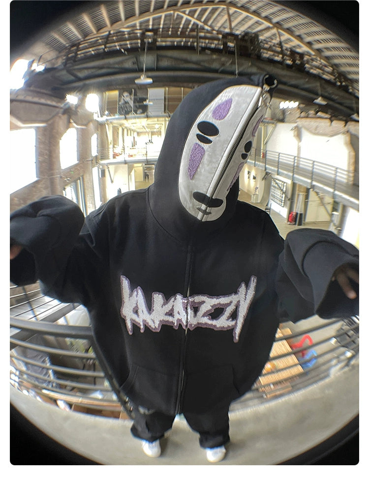 Someone indoors is wearing a Spirited Away No-Face Anime Hoodie, an oversized 400GSM zip-up sweatshirt with "Krazy" on it. Their face is hidden by a white oval mask with black and purple markings, set against an industrial backdrop ideal for anime fans.