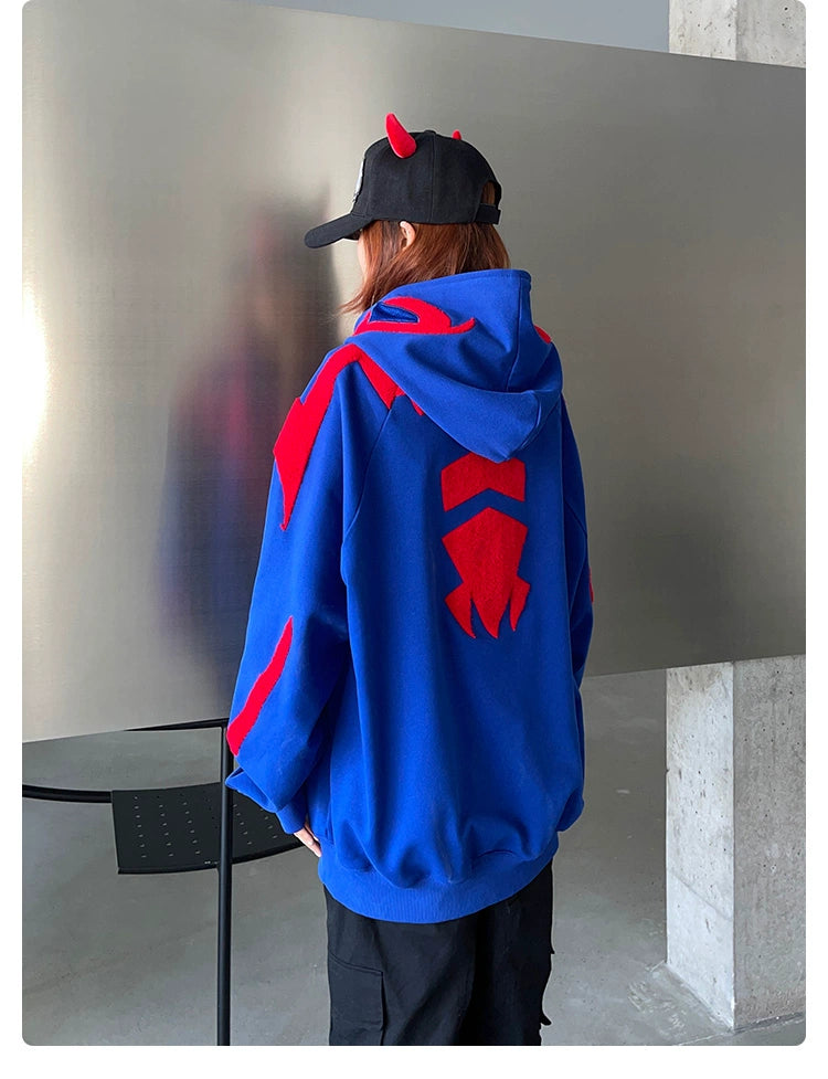 Dressed in a Seakoff Superhero Spider Hoodie, an oversized blue and red zip-up sweatshirt for fans, and a black cap with red horns, the person faces a reflective surface. The room&